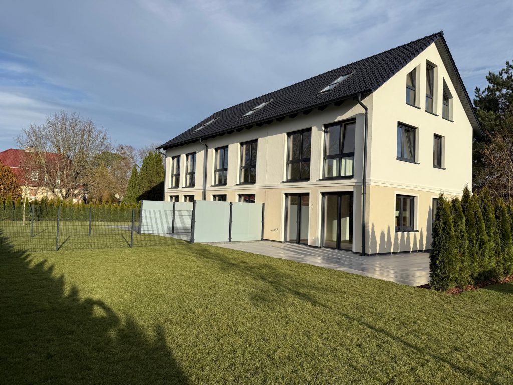 Seitliche Ansicht eines hellen Wohnhauses mit Gartenzaun