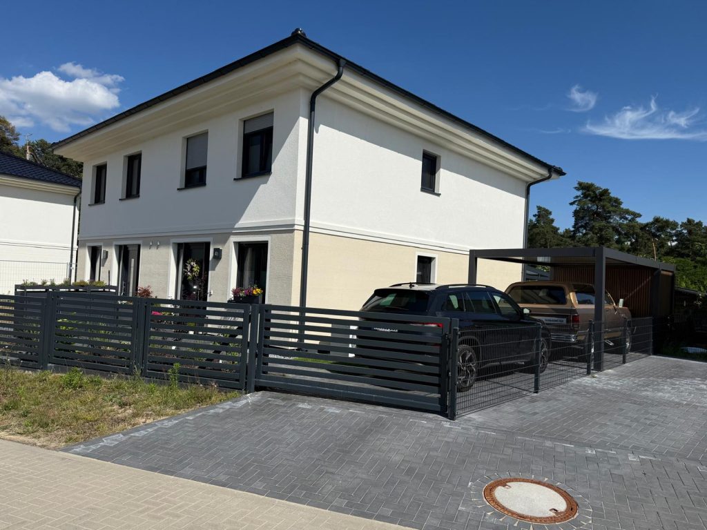 Neubau mit heller Fassade und dunklem Gartenzaun